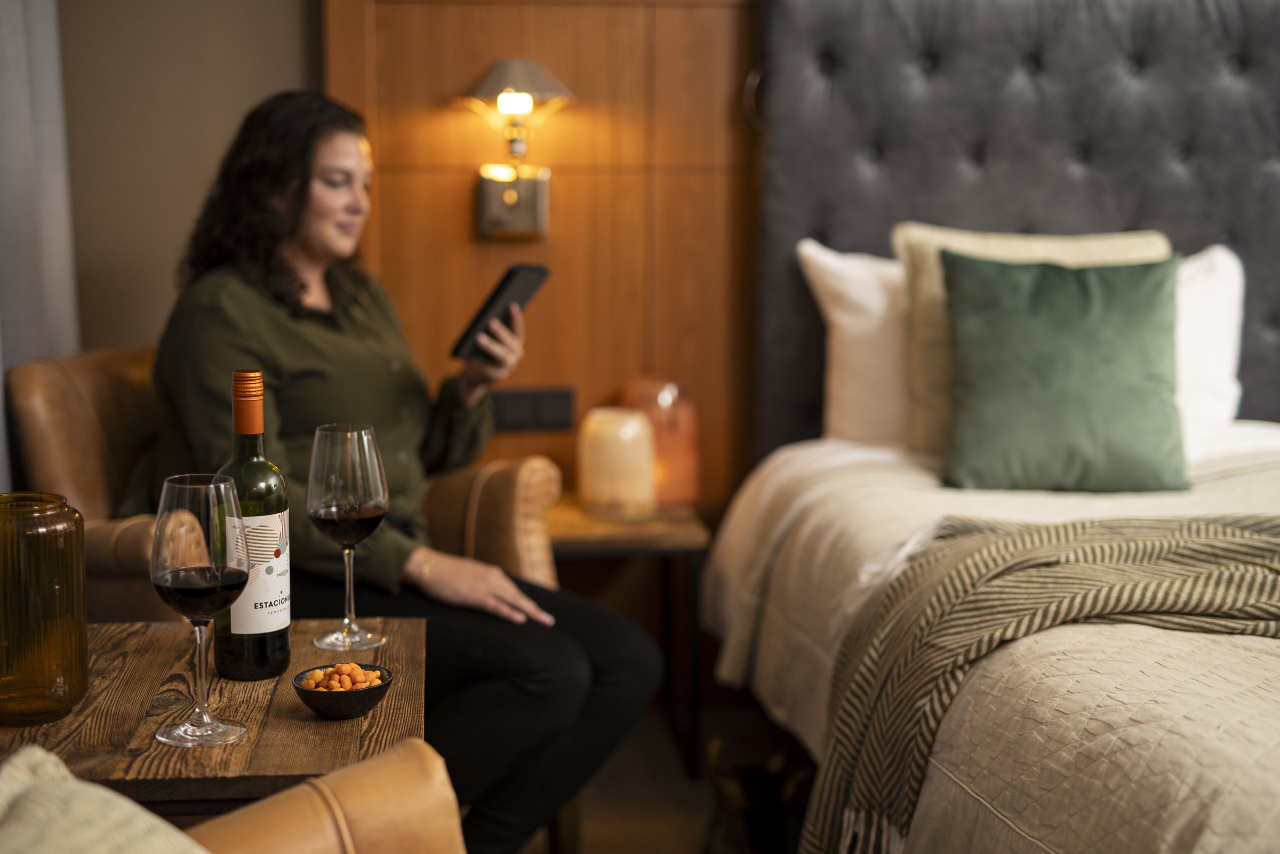 Een vrouw in een hotelkamer met haar e-reader en rode wijn.