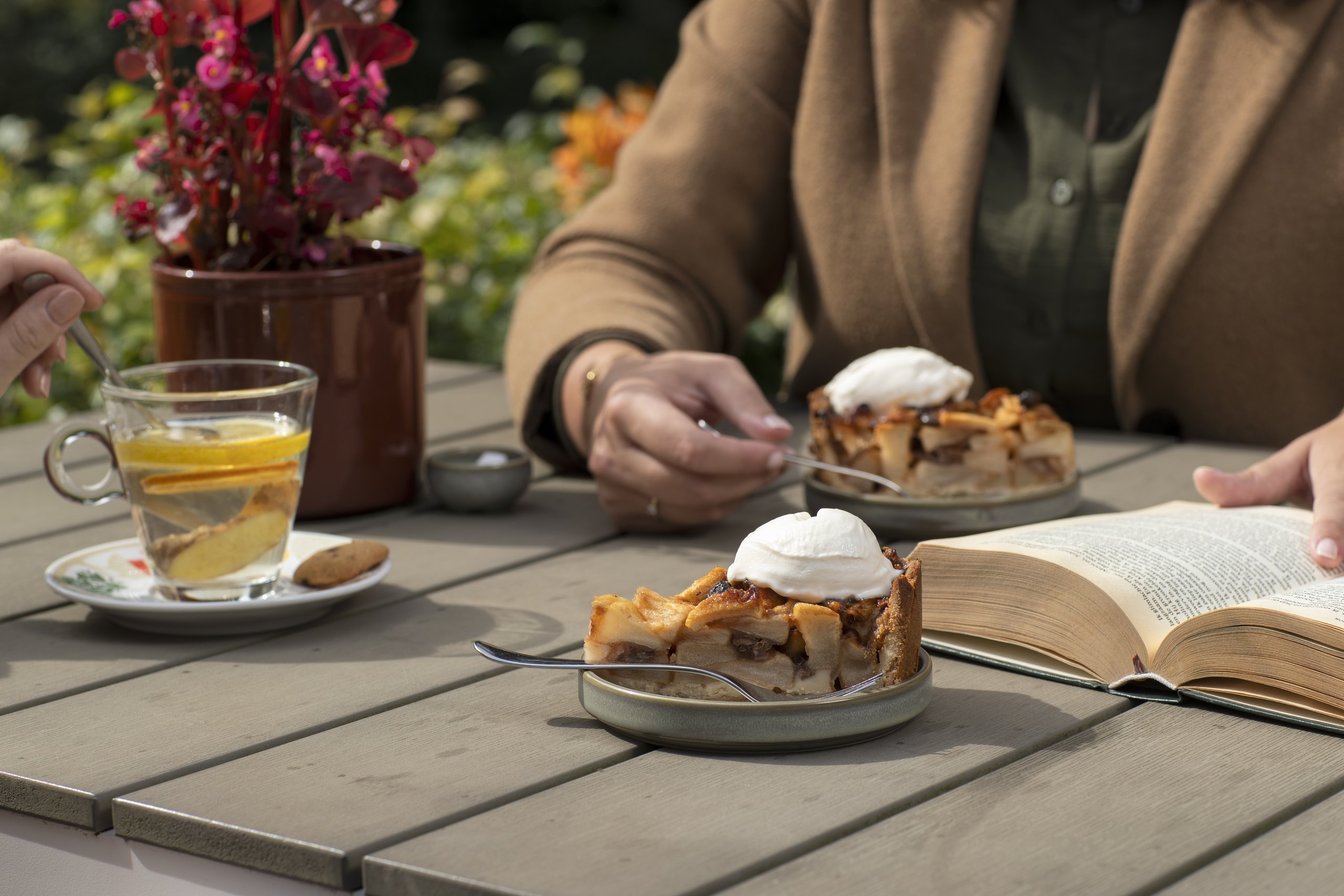 Een terrastafel gedekt met appeltaart met slagroom en een kop gember thee.