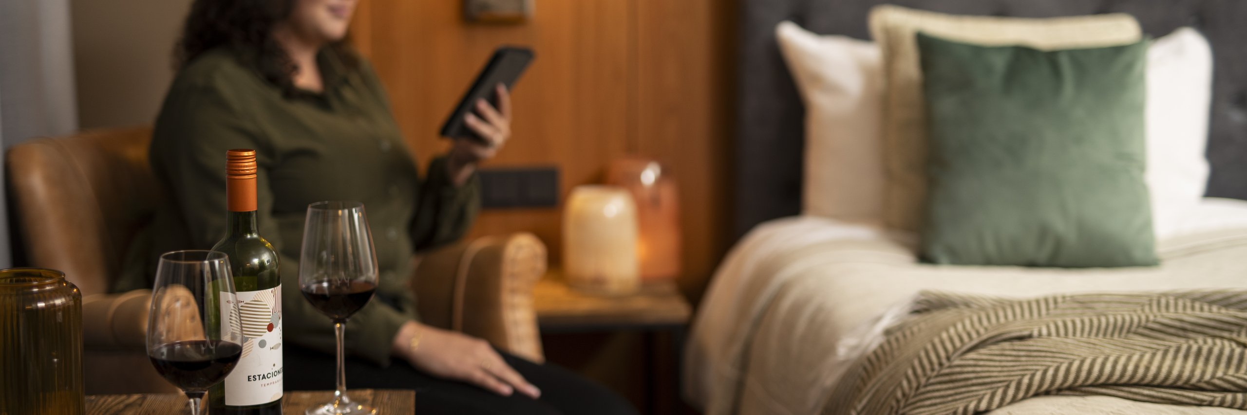 Een vrouw in een hotelkamer met haar e-reader en rode wijn.