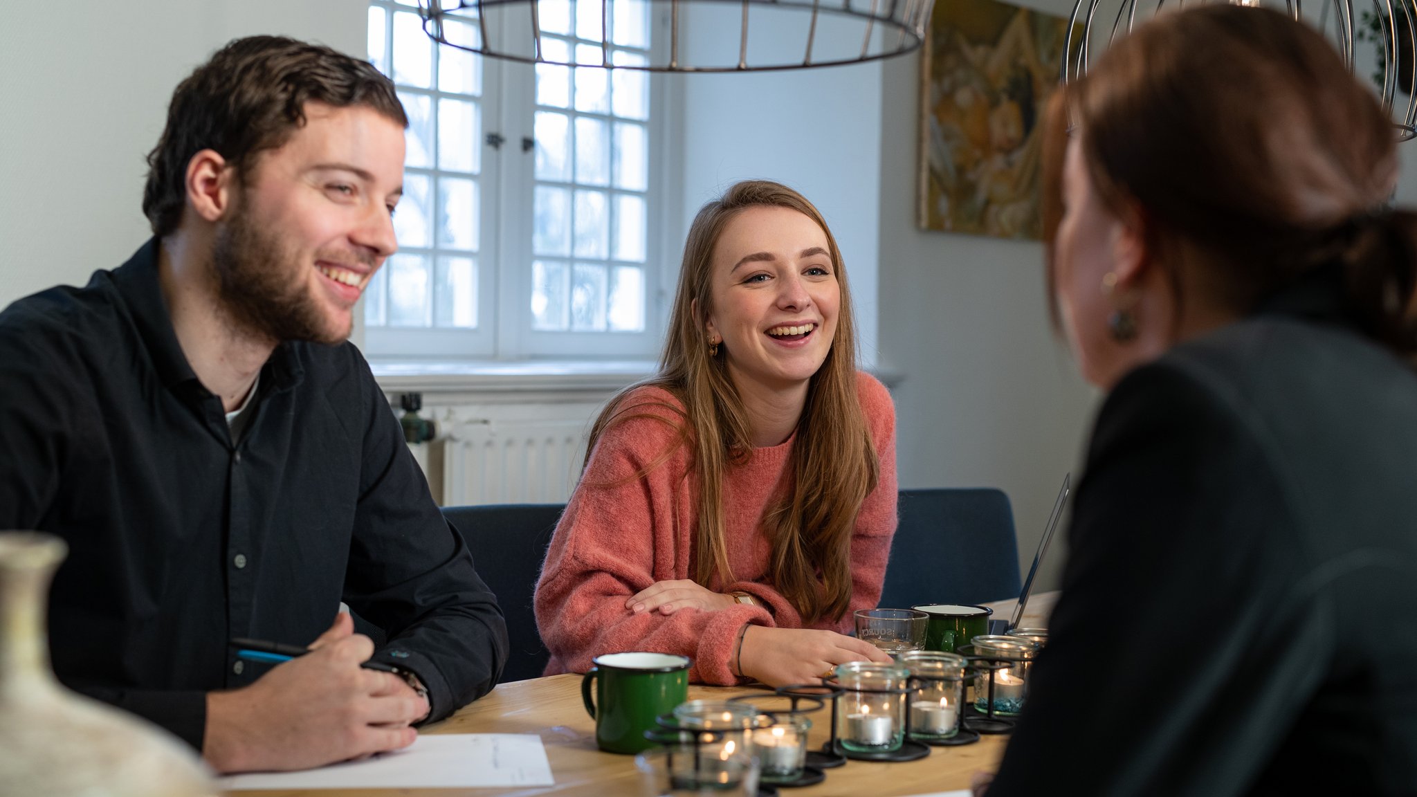 Drie lachende mensen aan de vergadertafel